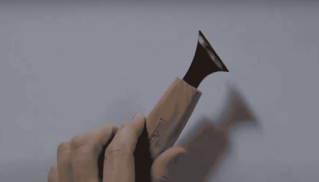 A close-up of a hand holding a curved wood carving tool. The tool has a wooden handle and a sharp, flat blade, ready for use in wood carving projects. Perfect for those interested in wood carving classes or lessons!